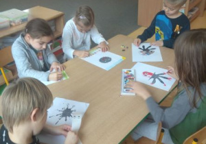 Dzieci przy stoliku przekształcają kleksy z atramentu