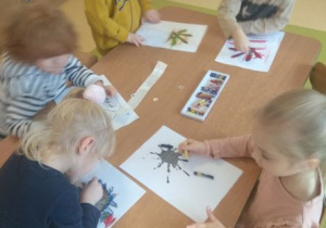 Dzieci przy stoliku przekształcają kleksy wykonane z atramentu