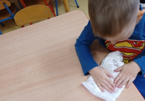 Gabryś wykonuje ćwiczenie sensoryczne, ugniata piankę do golenia zamkniętą w woreczku strunowym