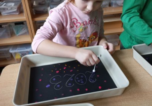 Hania stempluje wacikiem kolorowe kropki na czarnym papierze