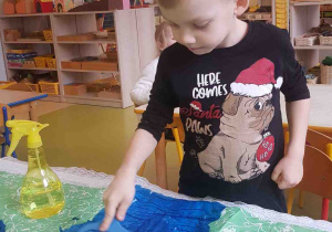 Chłopiec przygotowuje tło pracy przy użyciu mokrej bibuły i wałka plastycznego