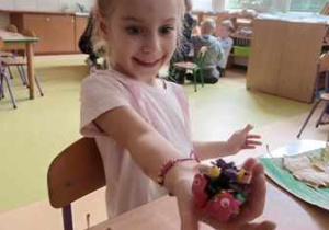 Anielka pozuje do zdjęcia z położonym na dłoni ślimakiem wykonanym z plasteliny oraz szyszki