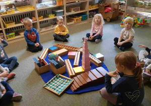 Dzieci siedzą na dywanie wokół montessoriańskiego materiału rozwojowego