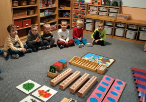 dzieci siedzą na dywanie przed montessoriańskim materiałem rozwojowym