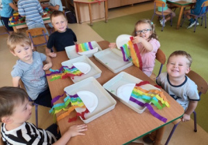 Dzieci siedzą przy stoliku i nazywają poszczególne kolory bibuły doklejonej przez siebie do papierowego talerzyka