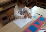 Dziewczynka siedzi przy stoliku i pracuje z metalowymi ramkami