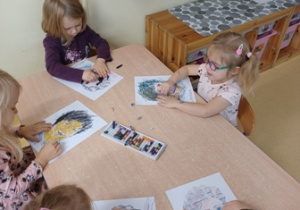 Dzieci siedzą przy stoliku i rysują portrety Marii Montessori