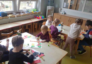 Dzieci przy stolikach, naklejają wycięte elementy