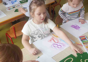 Dzieci siedzą przy stołach, korzystają podczas pracy z tabliczek z cyframi z papieru ściernego