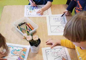 Dzieci siedzą przy stoliku i kolorują obrazki z parasolem