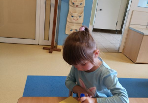 Dziewczynka siedzi przy stoliku i przykleja kolorowe kartki