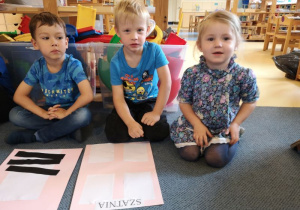 Dzieci siedzą na dywanie przed wykonaną przez siebie pracą plastyczną