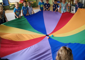 Dzieci podczas zabawy z chustą animacyjną próbują wrzucić piłki do otworu w chuście