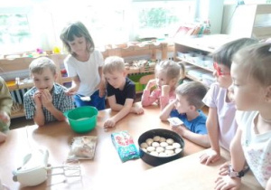 Chłopiec kładzie łyżkę serka do miski, pozostałe dzieci obserwują