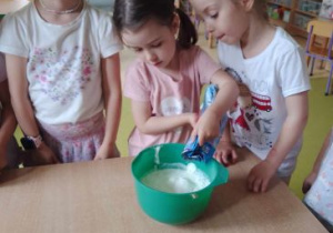 Dziewczynki obserwują czy ich koleżanka wsypuje prawidłową ilość składnika ciasta