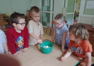 Dzieci stojące obok Natana sprawdzają czy prawidłowo odmierza serek