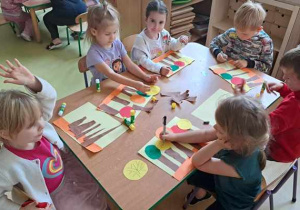 Dzieci siedzą przy stoliku podczas tworzenia jesiennej kompozycji z elementów kolorowego papieru