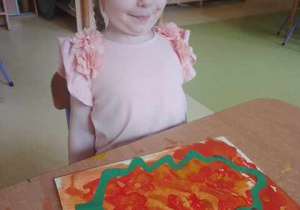 Zosia siedzi przy stoliku i podziwia swoją pracę plastyczną zrobioną z okazji "Dnia Spadającego Liścia"