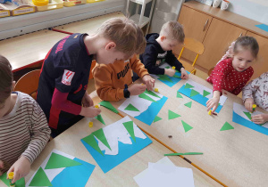 Dzieci przyklejają elementy zimowej pracy plastycznej