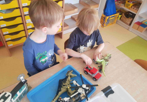 Chłopcy siedzą przy stole i bawią się modelami dinozaurów z Lego