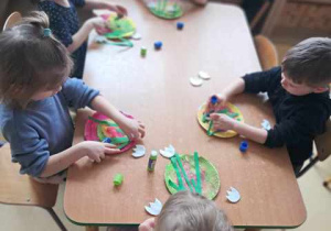 Dzieci w czasie wykonywania pracy plastycznej doklejają elementy do papierowego talerzyka tworząc przebiśniegi