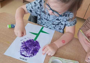 Chłopiec podczas wykonywania pracy plastycznej maluje hiacynta patyczkami higienicznymi zamoczonymi w fioletowej farbie