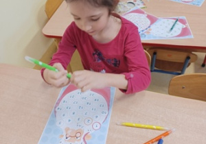 Dziewczynka siedzi przy stoliku i rysuje mazakami