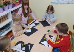 Dzieci w trakcie pracy plastycznej - przyklejania choinek z serwetek i gwiazd z papieru