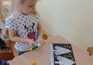 Hania smaruje klejem żółte gwiazdki i przykleja na ciemną kartkę