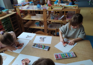 Dziewczynki siedzą przy stole i rysują Janusza Korczaka