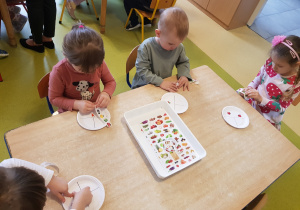 Dzieci przyklejają na talerzyki naklejki przedstawiające owoce, warzywa, węglowodany i nabiał
