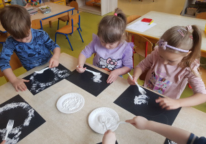 Dzieci stemplują karton białą farbą z wykorzystaniem widelca