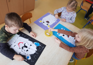 Dzieci stemplują śnieg na kartonie, korzystając z patyczków higienicznych