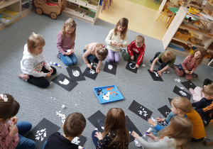 Dzieci siedzą na dywanie i wykonują wydzierankę z pingwinem