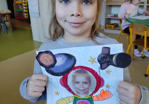 Dziewczynka prezentuje pracę plastyczną: ,,Ja w kosmosie".