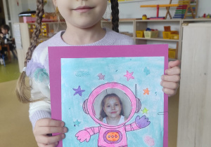 Dziewczynka prezentuje pracę plastyczną: ,,Ja w kosmosie".
