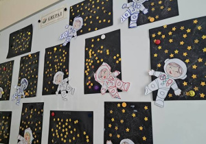 Wystawa prac dzieci z grupy I na tablicy w szatni przedszkolnej prezentująca prace plastyczne pt. "Astronauta w galaktyce"