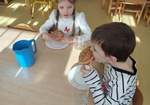 Dzieci siedzą przy stoliku i jedzą pączki