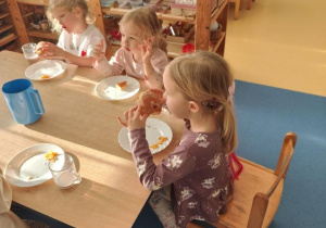Dzieci siedzą przy stoliku i jedzą pączki