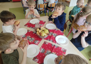 Dzieci siedzą przy wspólnym stole i zjadają pączki.