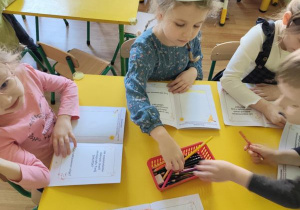 Dzieci siedzą przy stolikach i wykonują rysunki w swoich książeczkach