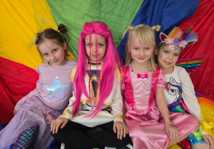 Dziewczynki w strojach karnawałowych siedzą na kolorowej chuście