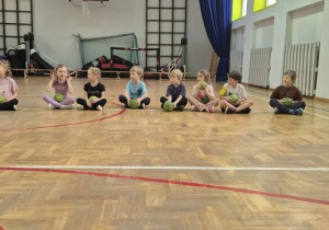 Dzieci siedzą skrzyżnie obok siebie i trzymają piłki w dłoniach