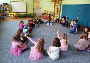 Dzieci siedzą na dywanie w kręgu i słuchają animatora
