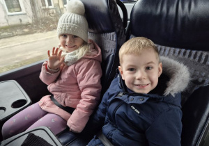 Chłopiec z dziewczynką siedzą w autokarze i machają ręką