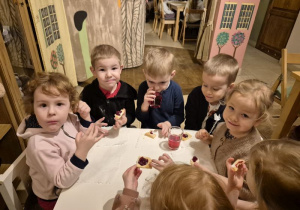 Dzieci siedzą przy stoliku i jedzą ciasteczka