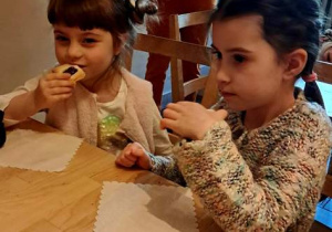 Dwie dziewczynki siedzą przy stoliku w "Baśniowej Kawiarence" i jedzą ciasteczka