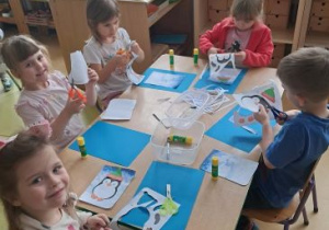 Dzieci siedzą przy stoliku podczas wykonywania działań plastycznych