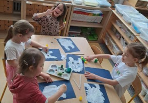 Dzieci siedzą przy stoliku i stemplują sylwetę niedźwiedzia