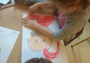 Dziewczynka rysuje kredkami pastelami Świetego Mikołaja.